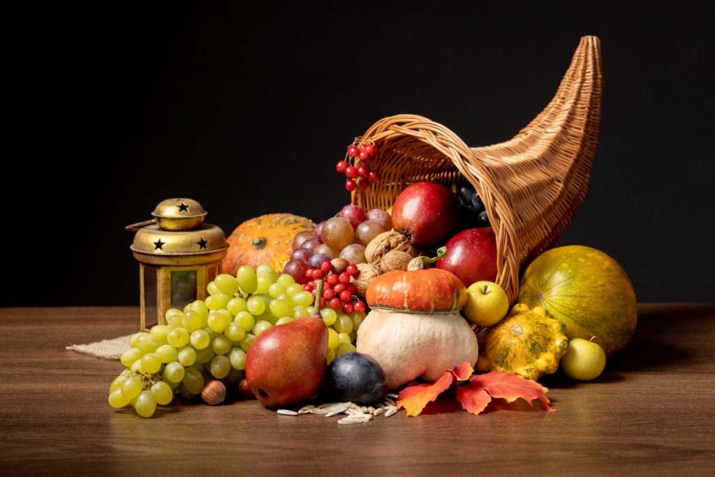 A Cornucopia filled with fruits and vegetables lies upon a table with a lantern decorated with stars.